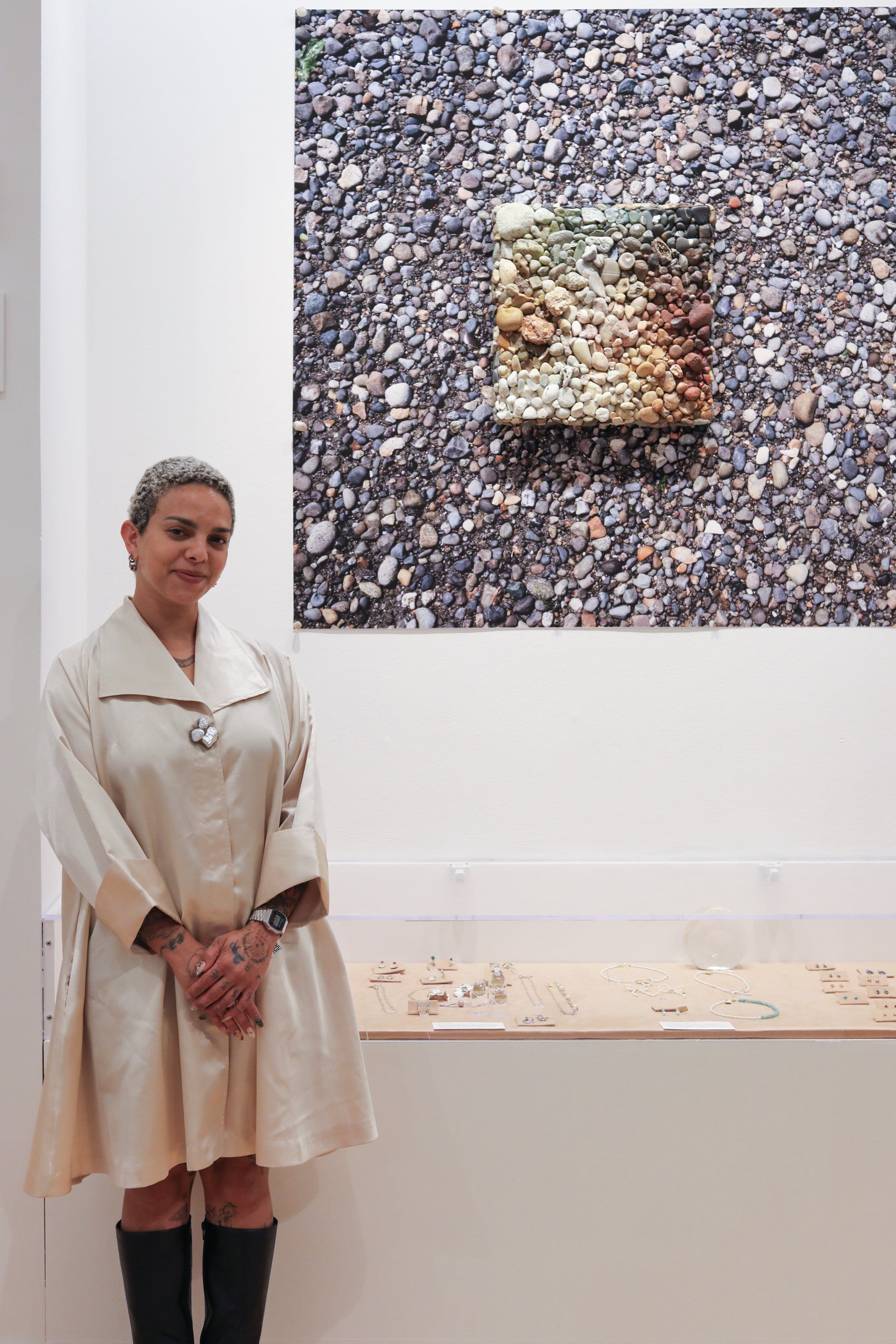 Person in a white coat standing in front of an art installation with pebbles.