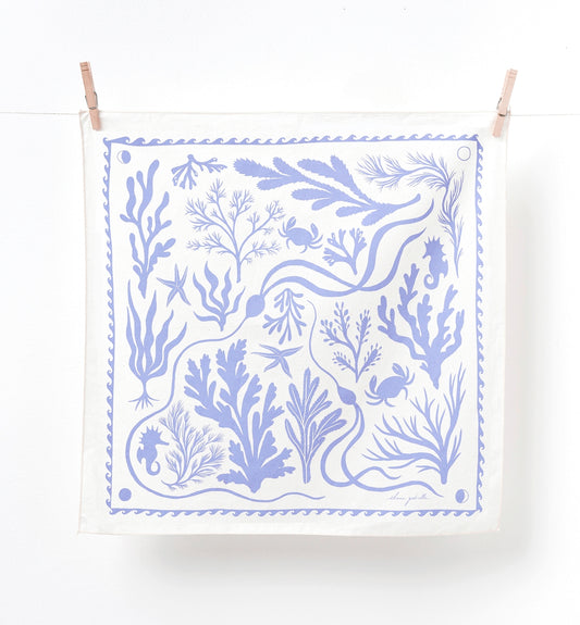 A square white fabric tea towel or bandana featuring a light blue botanical and nautical print, hanging from two wooden clothespins on a white string against a white wall.